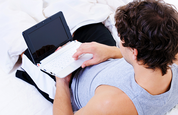 Casual young man lying in bed with a laptop - high angle view